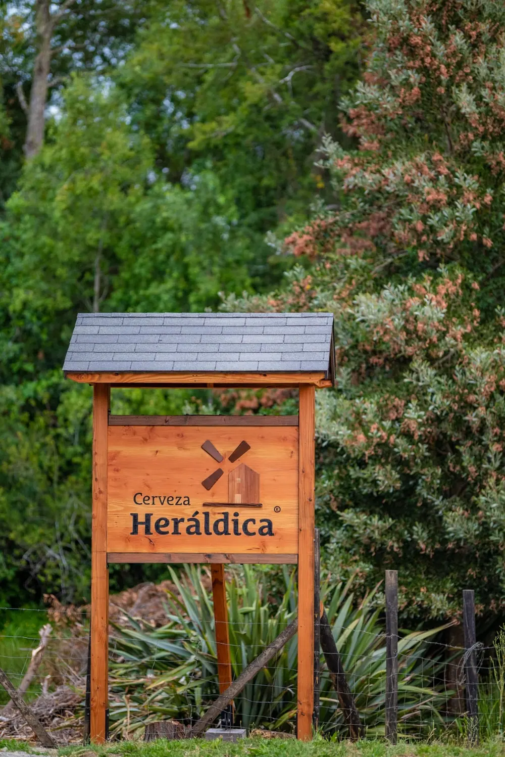 Letrero de madera de Heráldica entre la vegetación, en la entrada de la cervecería